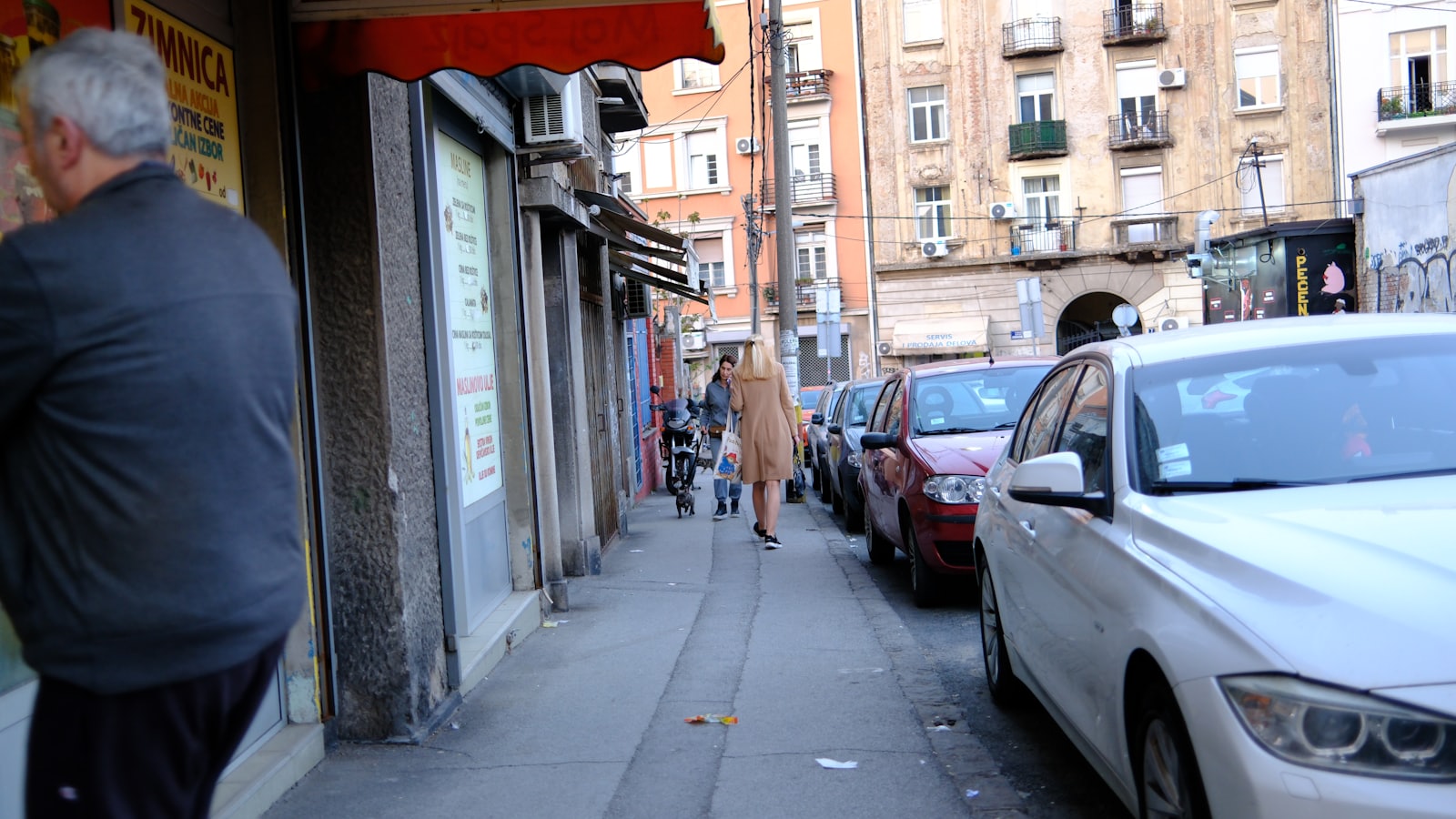 People walking on a sidewalk next to parked cars.