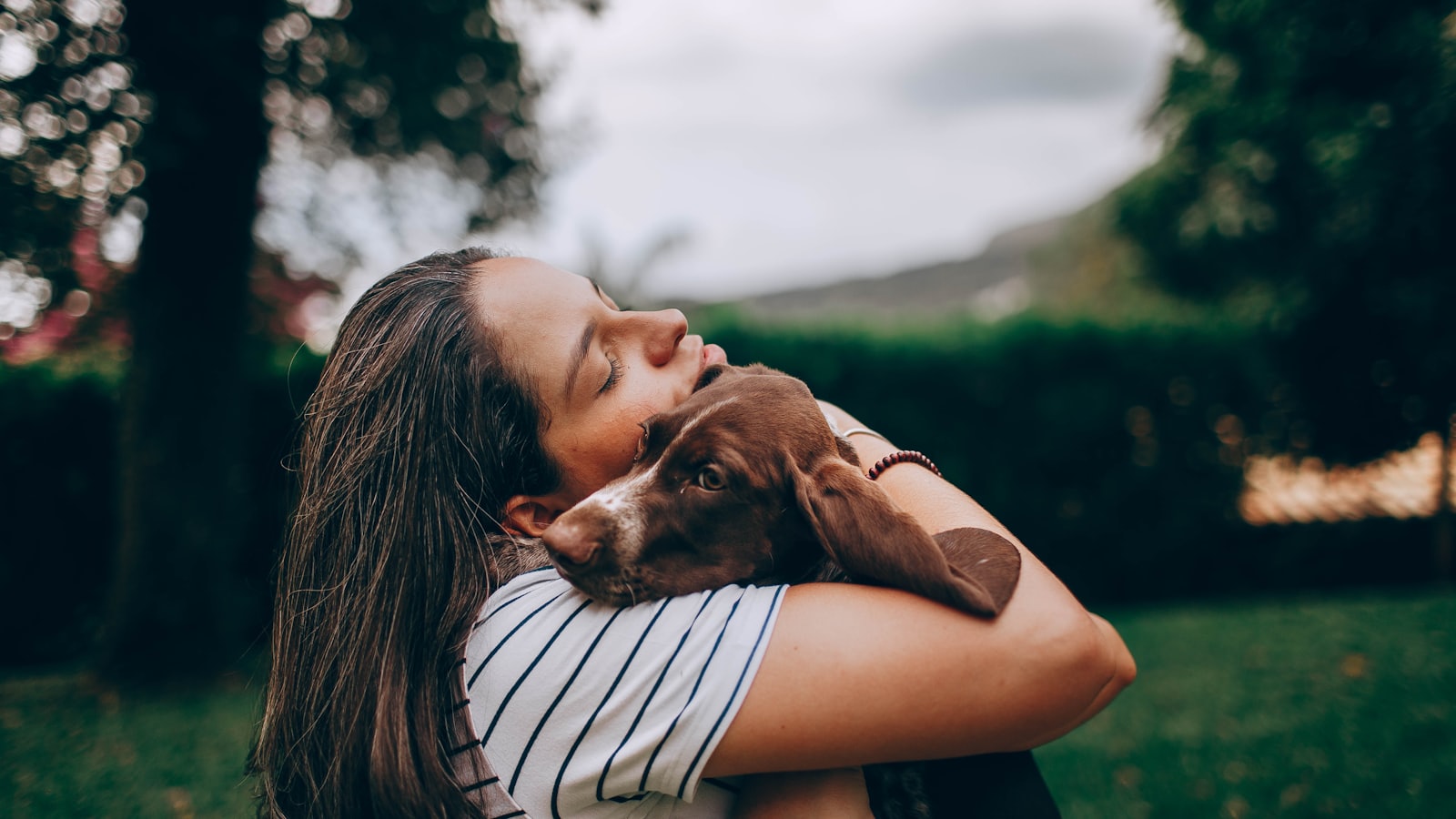 woman in white and black stripe shirt hugging brown short coated dog