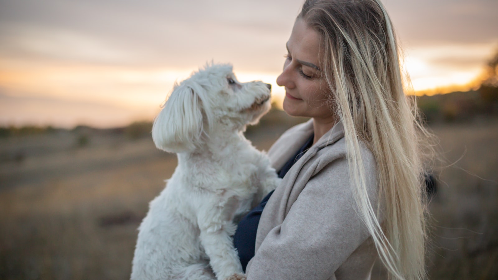 a woman holding a white dog in a field