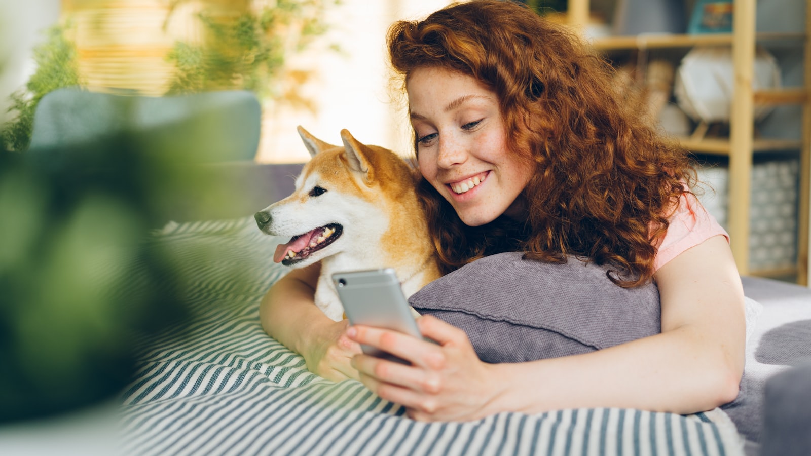 a woman laying on a bed with a dog looking at a cell phone